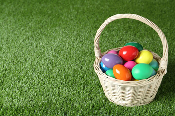 Wicker basket with Easter eggs on green grass. Space for text