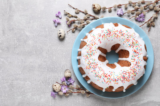 Glazed Easter cake with sprinkles, quail eggs, flowers and willow branches on light table, flat lay. Space for text