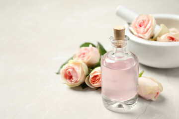 Fototapeta na wymiar Bottle of rose essential oil and flowers on white table, space for text