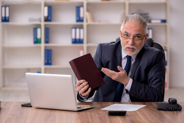 Old male employee holding book at workplace