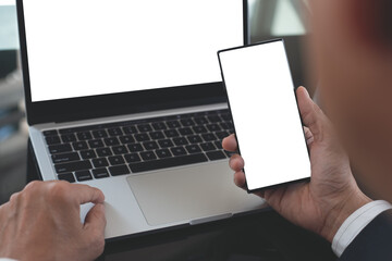 Mockup image, business man hand holding black black mobile smart phone working on laptop computer at office