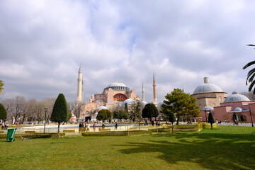 Fototapeta na wymiar Turkey istanbul 03.03.2021. Facade and outside of Hagia sophia mosque now,before museum and ancient church from sultanahmet square with tourist palm trees during blue overcast sky background. 