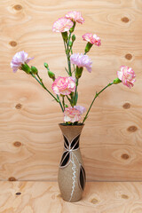 Beautiful Japanese carnation flower arrangement in small ceramic vase. Wood background. Copy space. Vertical shot.