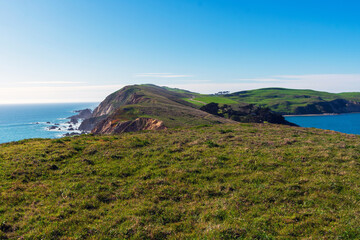 Fototapeta na wymiar View of Pacific Ocean coastline, with winter green grass covering cliffs and bluffs of Point Reyes Headlands on a sunny day at Point Reyes National Seashore, California.