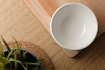 White empty bowl with wood cutting board as background and plant as foreground