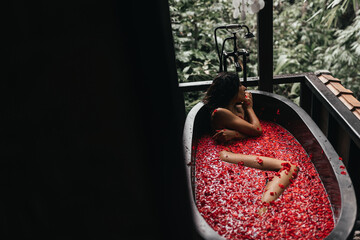 Woman relaxing in round outdoor bath with tropical flowers, organic skin care, luxury spa hotel, lifestyle photo