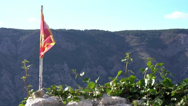 Red flag of Montenegro with golden double headed eagle placed on top of mountain flutters in the wind, beautiful sunny day. Old tradition of conquering the top.