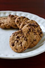 A close up shot of some delicious homemade chocolate chip cookies on a white ceramic plate.