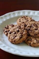 A close up shot of some delicious homemade chocolate chip cookies on a white ceramic plate.