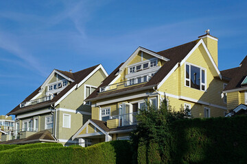 Row of pastel colored clapboard houses with upper level balconies and evergreen hedges