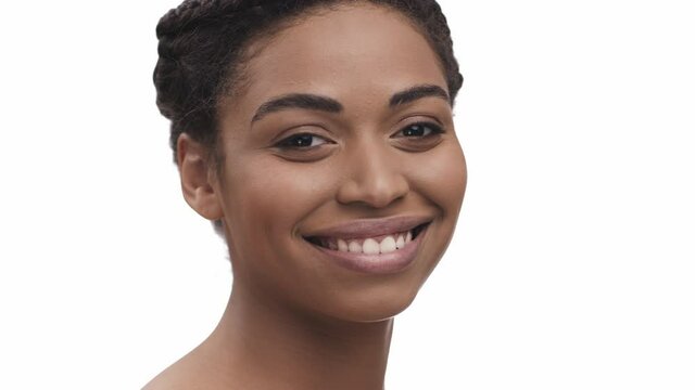Close up of beautiful african american woman turning face to camera and smiling widely, white studio background