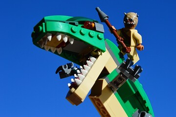 Obraz premium LEGO Star Wars Tusken Raider riding on Tyrannosaurus Rex from LEGO Creator series, blue skies background.