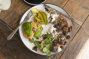 High angle view of lunch plate with avocado, mushrooms and toast on wooden table (selective focus)