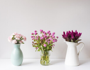 Close up of three vases of flowers on white table against wall (selective focus)