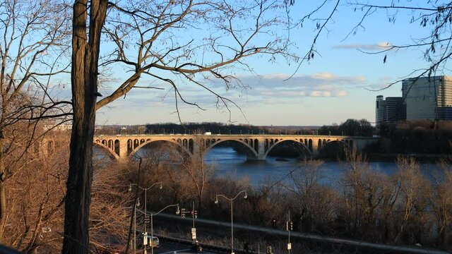 Francis Scott Key Bridge, which connects Georgetown in Washington, DC to Rosslyn, Virginia. Seen on a winter evening from the DC side of the Potomac River. Leafless trees line the river.