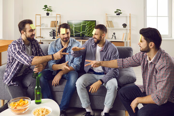 Bunch of adult friends having a party and enjoying fun time together. Group of young men sitting on sofa at home and playing Rock Paper Scissors and Who Am I games. Free time, leisure and lifestyle
