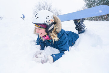 Portrait of a girl snowboarder in the snow. A girl in a ski helmet and a jacket lies on the snow.