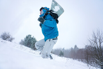 The guy snowboarding goes on a snowy slope. He is holding a snowboard