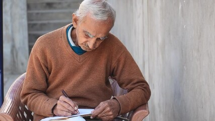 Portrait of Indian senior businessman writing in diary while sitting on chair at home. Old people hobby concept.  - Powered by Adobe