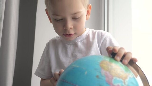 boy studies globe. education travel tourism lifestyle concept. child twists the globe sits on a window sill. kid looking for a country on a globe map. world map geography study