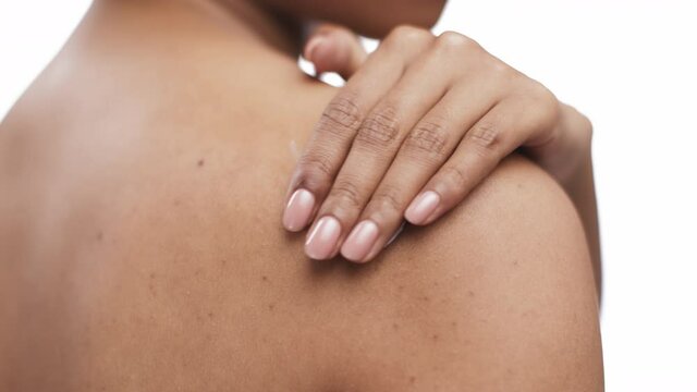 Body care. Close up of black woman applying pampering lotion on her shoulder skin after shower, slow motion