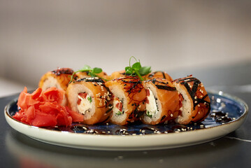 A close-up photo of fresh sushi rolls with salmon, Philadelphia cheese, and tuna on a blue ceramic plate with sauce, sesame, and wasabi. Black stone table