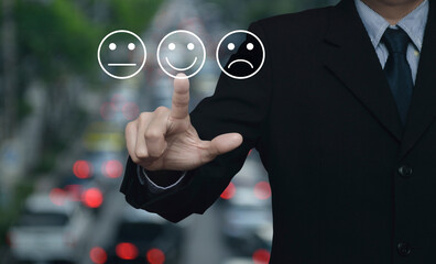 Businessman pressing excellent smiley face rating icon over blur of rush hour with cars and road in...