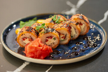 Sushi rolls with salmon, Philadelphia cheese, and tuna on a blue ceramic plate with sauce, sesame,  wasabi, and leaves. Black stone table.