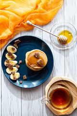 Homemade pancakes with honey, banana and chocolate. Healthy breakfast concept, copy space. A bright still life with a cup of tea, a plate of pancakes and interesting shadows.