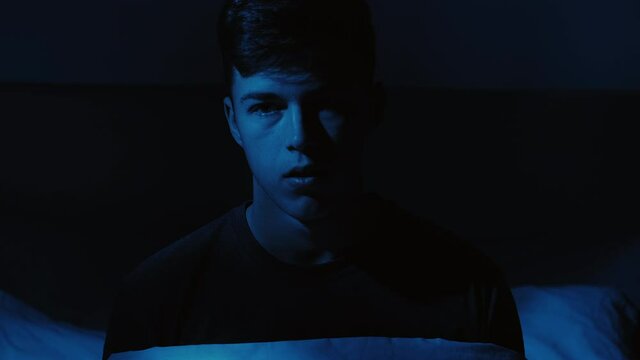 Nightmare fear. Scary dream. Panic attack. Disturbed frightened shocked guy raised up in bed fell asleep late at home in dark blue light.