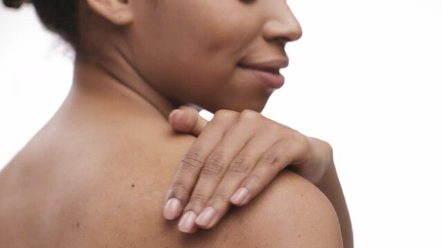 Close up of young african american lady applying moisturizing cream on her shoulder skin, back view, slow motion