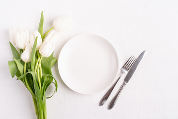 Festive table setting in white, white plate and tulips top view on background
