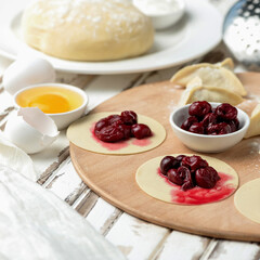 Cherry filling on rolling Raw dough circles on wooden board. Process of cooking dumplings. Ingredients to create homemade food or culinary masterpiece. Square format or 1x1 for social media posting.