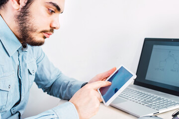 Young Entrepreneur at work, using tablet and laptop to work in his office.