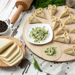Mozzarella cheese and dill filling on rolling dough circles. Ingredients and kitchen utensils with Rolling pin on wooden table. Process of cooking dumplings. Top view. Square format or 1x1.