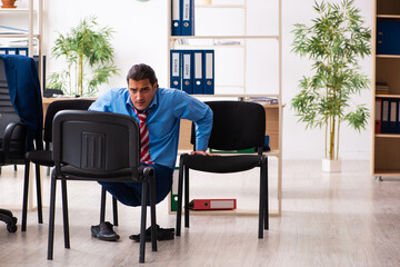 Young male employee doing sport exercises at workplace