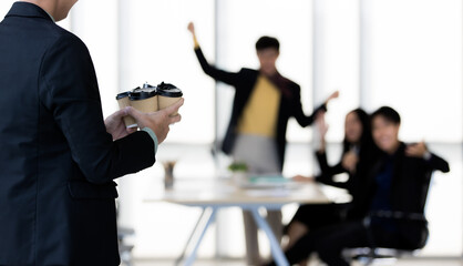 A man in suit brings cups of coffee into office and the colleagues feel happy and excited with beverage in relax time. Team support and unity of workplace concept