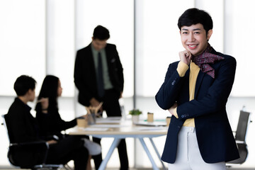 Portrait of LGBTQ transgender man office employee in casual suit standing and pose to camera with cheerful and happy gesture with team colleagues blur in background.