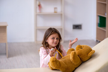 Small girl holding bear toy waiting for doctor in the clinic