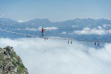 A person walks on a suspended rope bridge in the clouds. Extreme attraction. Wanderlust and adventures.