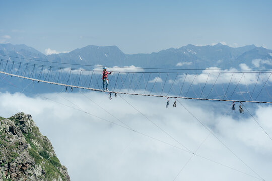 A Person Walks On A Suspended Rope Bridge In The Clouds. Extreme Attraction. Wanderlust And Adventures.