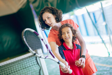 Young cute female coach teaching a boy to hold a tennis racket