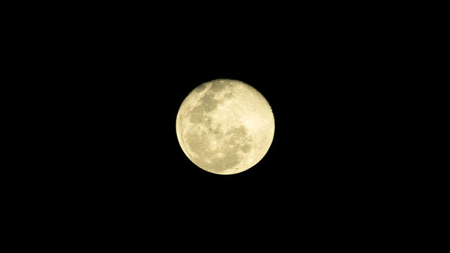 yellow almost full moon in dark sky at night, image shot with super telephoto lens