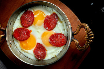Appetizing turkish breakfast dish - scrambled eggs with sujuk in a frying pan on a black background