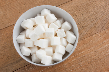 pieces of white sugar in a ceramic bowl on a light wooden background, selectively focused