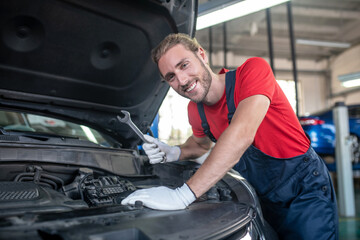 Smiling man with wrench near car hood