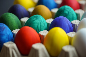 Fototapeta na wymiar Close up colorful painted eggs in cardboard stand for Easter on dark background. Multiple colors eggs. Easter concept
