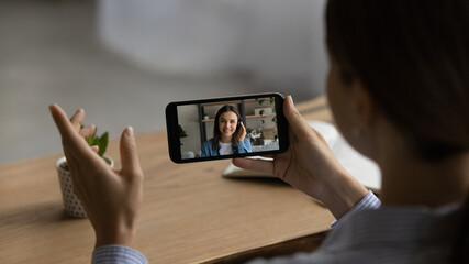 Close up of woman talk speak on video on smartphone with client or colleague. Back view of female...
