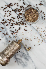 Organic dried Black Peppercorns and coarse ground  pepper in a  bowl on a marble background...