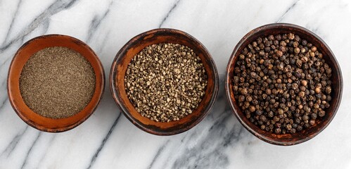Organic dried Black Peppercorns and peppers are coarse and fine ground in a clay bowls on a marble background close-up. Seasonings and spices.  Selective Focus, banner, long picture